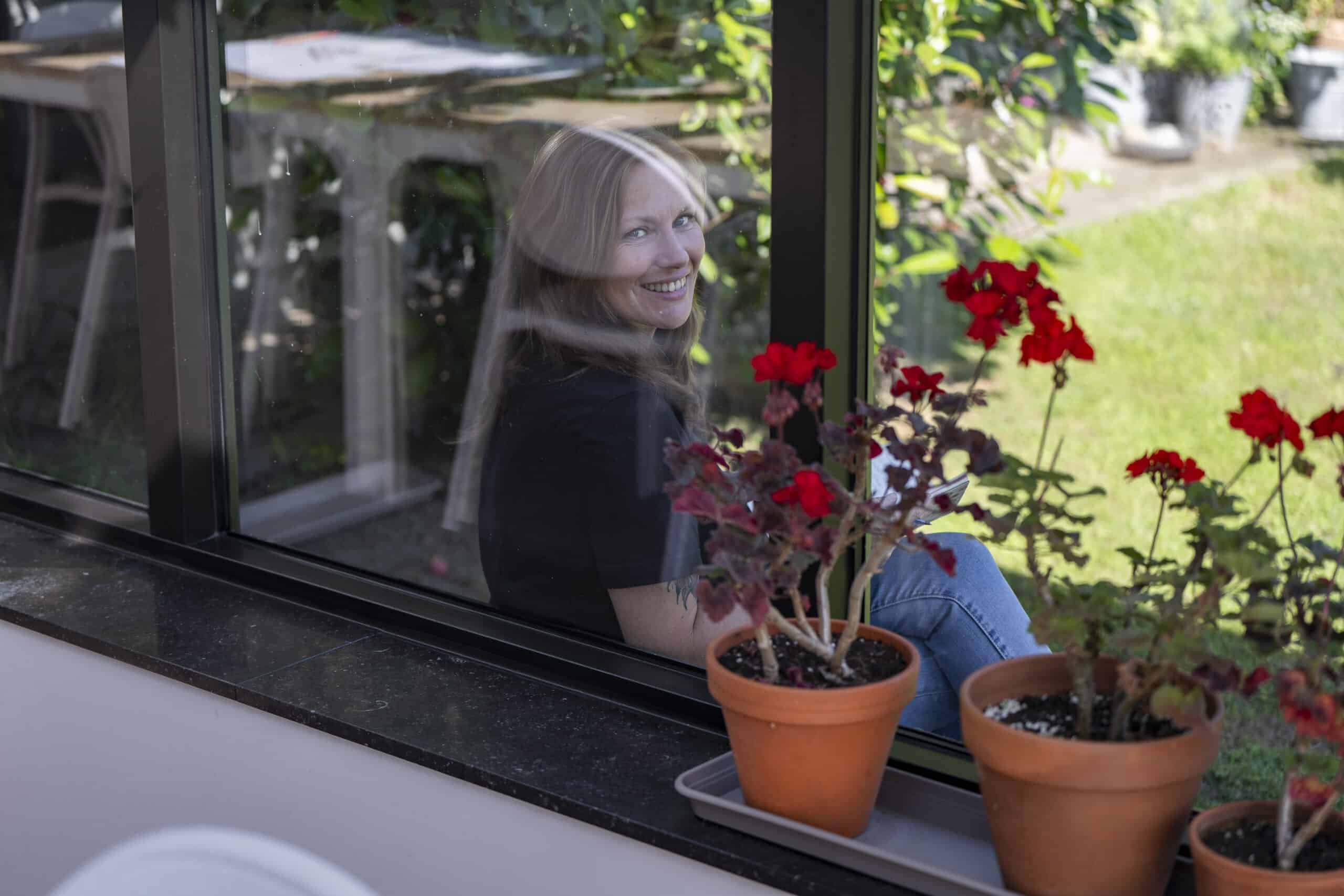 Linsey zit in de orangerie bij het raam samen met prachtige rode bloemen